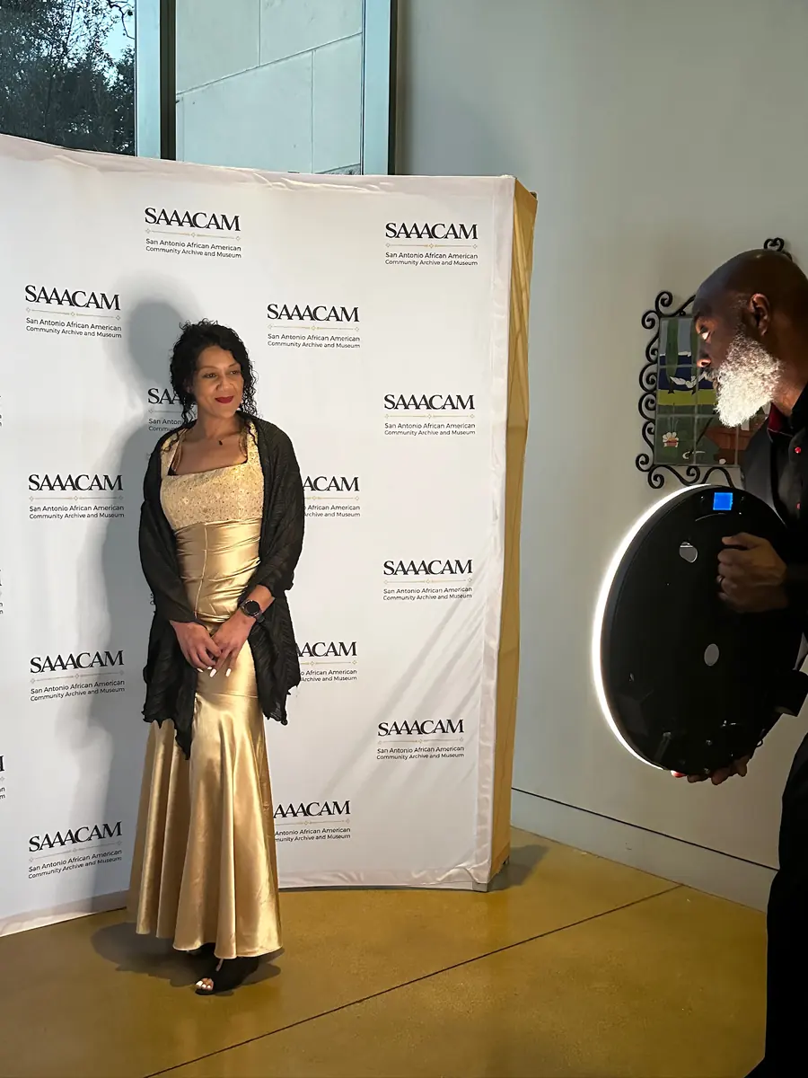 Guest in a gold gown posing at a gala backdrop while an attendant holds the ring-light booth